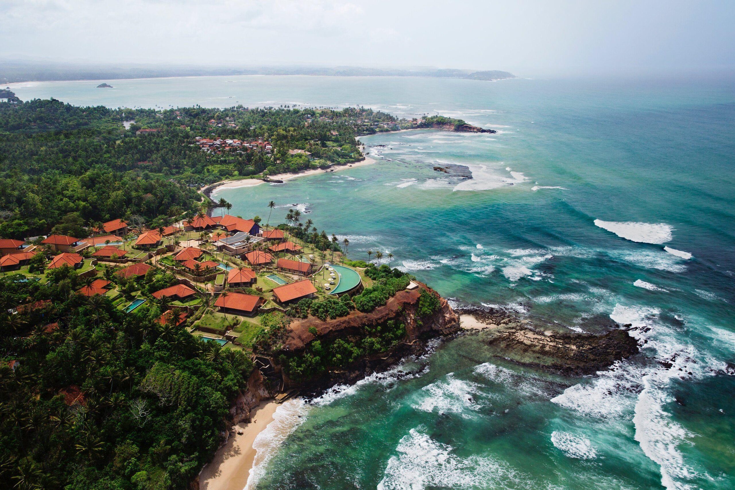 Aerial view of Sri Lanka’s southern coastline featuring turquoise waters, tropical vegetation, rocky shoreline, and a coastal resort overlooking the Indian Ocean.